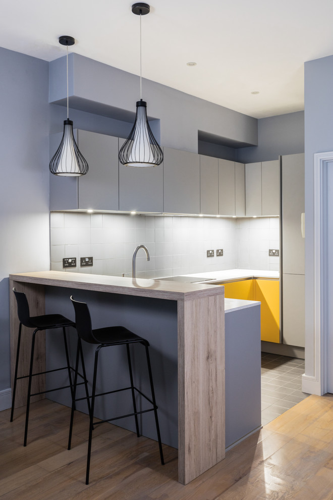 Immagine di una piccola cucina ad U contemporanea con ante lisce, ante grigie, parquet chiaro e pavimento beige