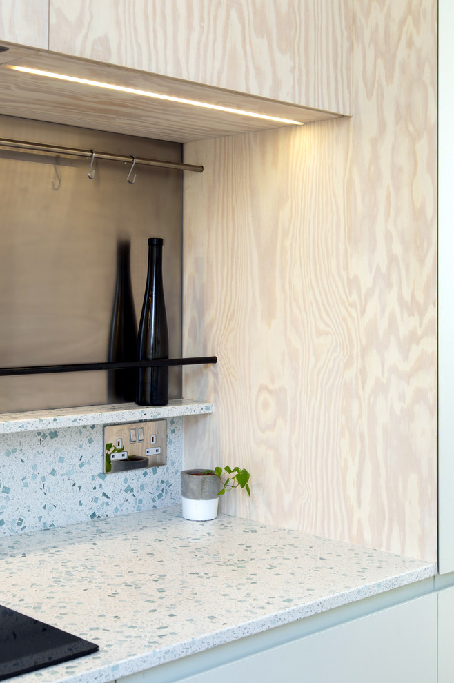 Bild på ett litet skandinaviskt vit vitt kök med öppen planlösning, med en enkel diskho, släta luckor, bänkskiva i återvunnet glas, vitt stänkskydd, rostfria vitvaror, mellanmörkt trägolv och en köksö