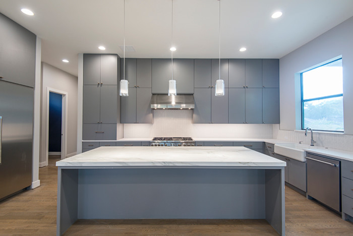 Inspiration for a modern kitchen in Houston with a belfast sink, flat-panel cabinets, grey cabinets, quartz worktops, grey splashback, stainless steel appliances, medium hardwood flooring and an island.