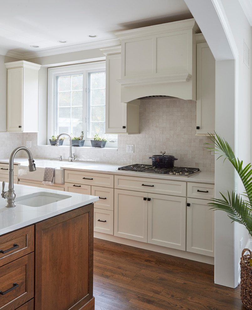 This is an example of a large classic open plan kitchen in San Francisco with a belfast sink, flat-panel cabinets, white cabinets, engineered stone countertops, white splashback, terracotta splashback, stainless steel appliances, medium hardwood flooring, an island and brown floors.