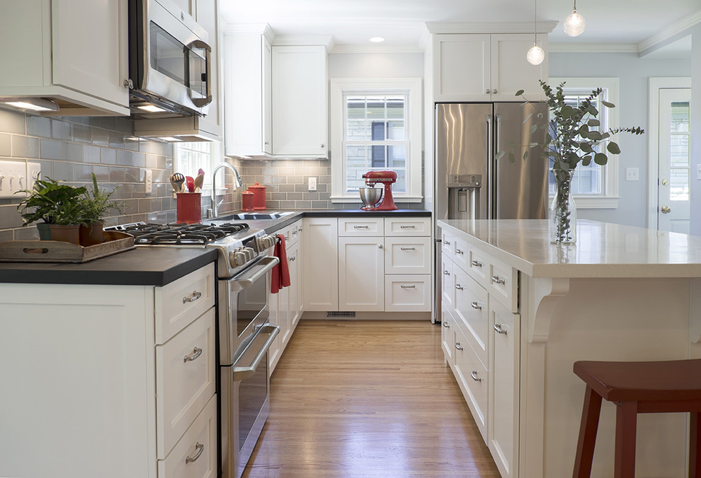 Example of a mid-sized transitional l-shaped medium tone wood floor eat-in kitchen design in Louisville with an undermount sink, shaker cabinets, white cabinets, concrete countertops, gray backsplash, ceramic backsplash, stainless steel appliances and an island
