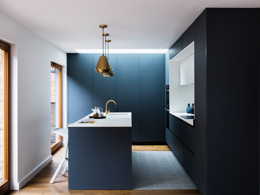 Inspiration pour une petite cuisine minimaliste en L avec un évier encastré, un placard à porte plane, des portes de placard bleues, une crédence blanche, un sol en bois brun, îlot et un sol marron.