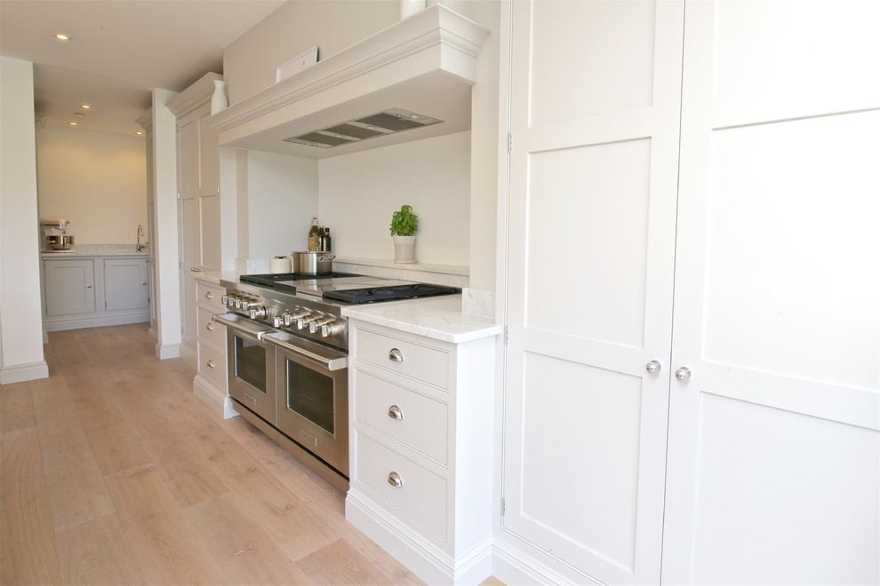 Design ideas for a large contemporary single-wall open plan kitchen in Surrey with shaker cabinets, beige cabinets, marble worktops, white splashback, stone slab splashback, stainless steel appliances, light hardwood flooring and an island.