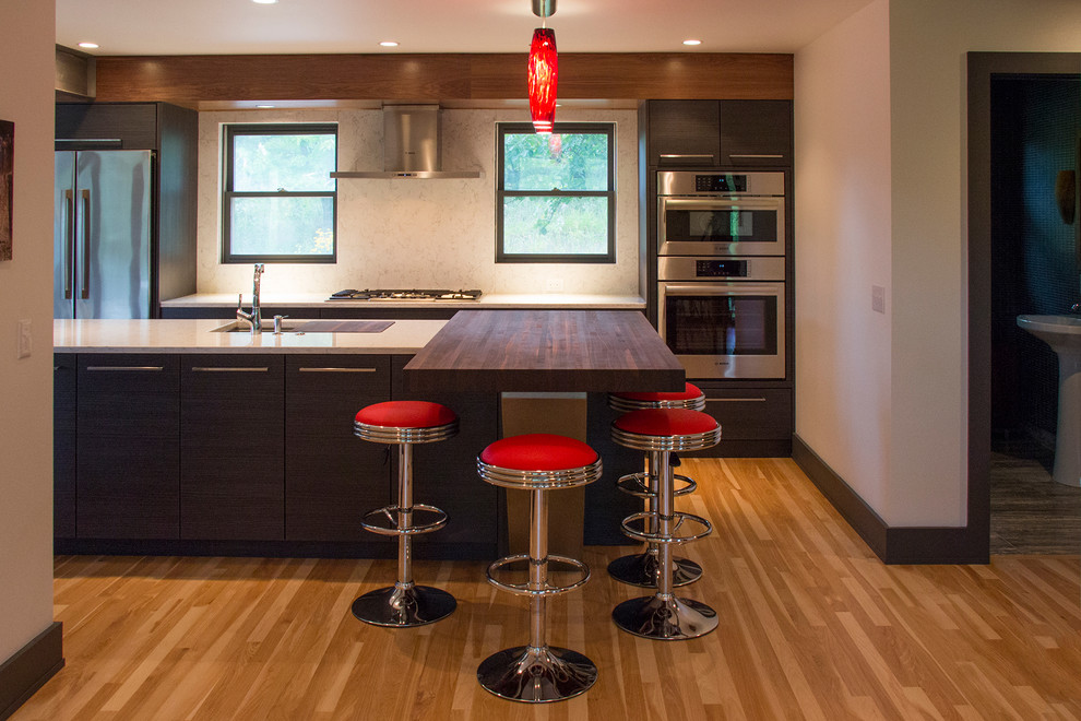 This is an example of a medium sized contemporary single-wall kitchen/diner in Milwaukee with a submerged sink, flat-panel cabinets, dark wood cabinets, engineered stone countertops, grey splashback, stone slab splashback, stainless steel appliances, light hardwood flooring and an island.