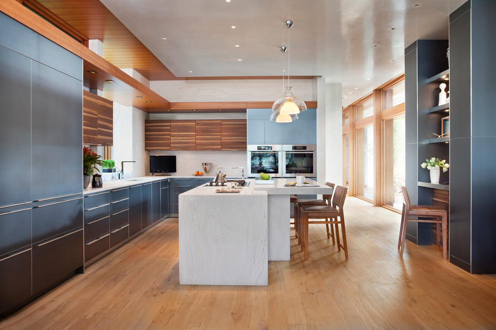 This is an example of a contemporary l-shaped kitchen in Minneapolis with a submerged sink, flat-panel cabinets, grey cabinets, white splashback, stainless steel appliances, medium hardwood flooring and an island.