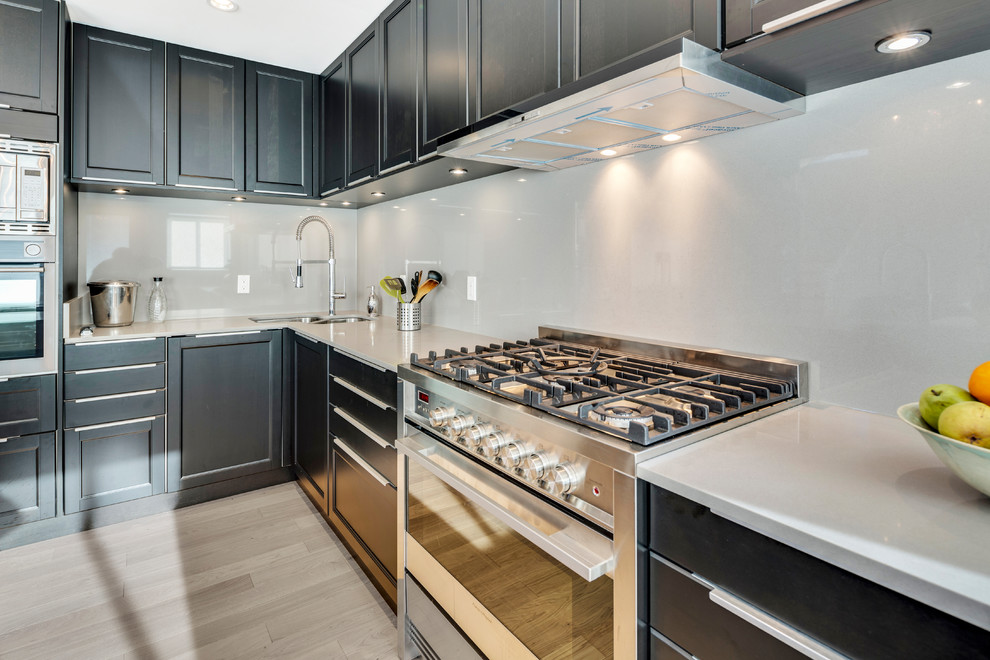 Foto på ett litet funkis kök, med en undermonterad diskho, skåp i shakerstil, svarta skåp, bänkskiva i kvartsit, grått stänkskydd, stänkskydd i sten, rostfria vitvaror, laminatgolv och en köksö
