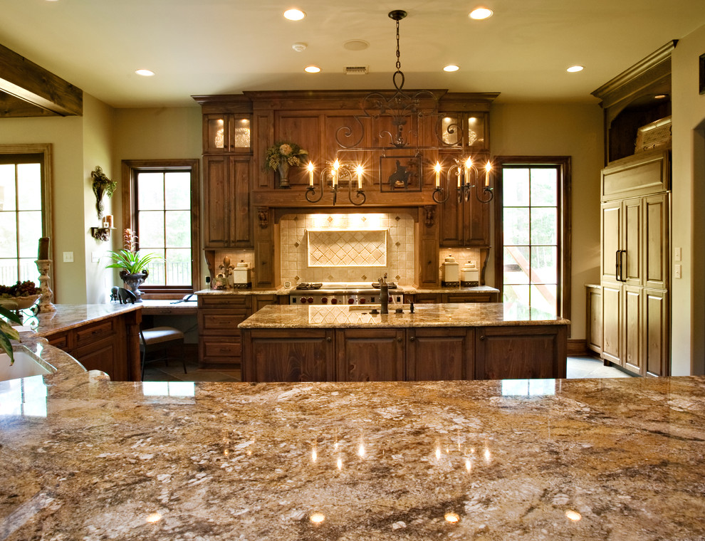 Example of a large classic l-shaped slate floor open concept kitchen design in New Orleans with beaded inset cabinets, medium tone wood cabinets, granite countertops, beige backsplash, stone tile backsplash, paneled appliances and two islands