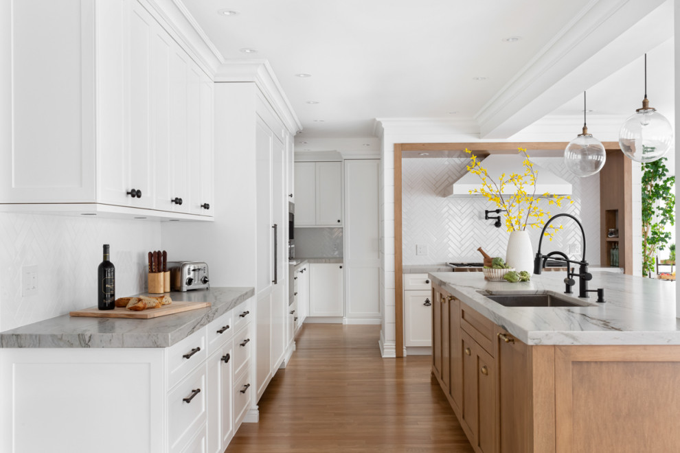 Design ideas for an expansive nautical l-shaped kitchen pantry in Montreal with a single-bowl sink, shaker cabinets, white cabinets, quartz worktops, white splashback, porcelain splashback, integrated appliances, light hardwood flooring, an island, brown floors and grey worktops.