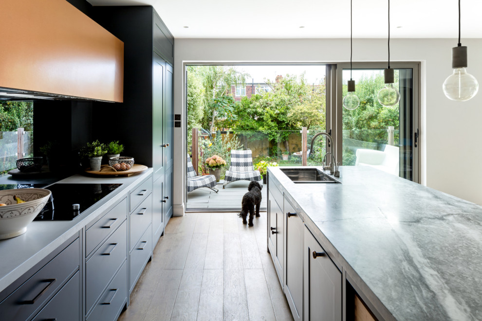 Foto på ett mellanstort funkis grå kök, med en nedsänkt diskho, släta luckor, blå skåp, marmorbänkskiva, blått stänkskydd, glaspanel som stänkskydd, svarta vitvaror, mellanmörkt trägolv, en köksö och brunt golv