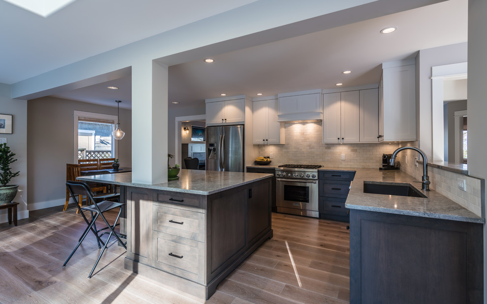 Eat-in kitchen - mid-sized traditional l-shaped medium tone wood floor and brown floor eat-in kitchen idea in Other with an undermount sink, shaker cabinets, white cabinets, white backsplash, stainless steel appliances, an island and gray countertops
