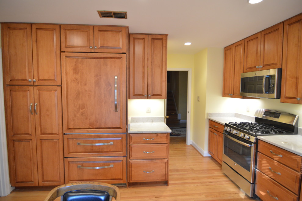 Klassisk inredning av ett mellanstort grå grått kök, med en enkel diskho, luckor med upphöjd panel, skåp i mellenmörkt trä, granitbänkskiva, integrerade vitvaror, ljust trägolv och beiget golv