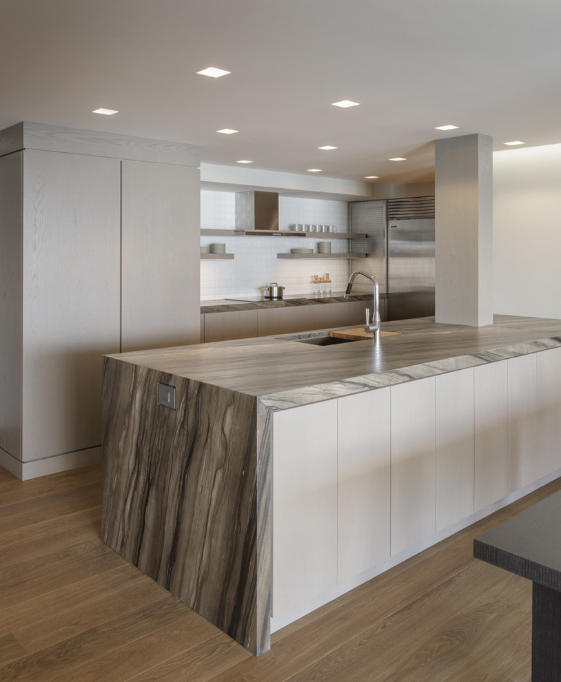 Design ideas for a modern l-shaped kitchen in Seattle with a submerged sink, flat-panel cabinets, light wood cabinets, white splashback, metro tiled splashback, stainless steel appliances, medium hardwood flooring, an island, brown floors and grey worktops.