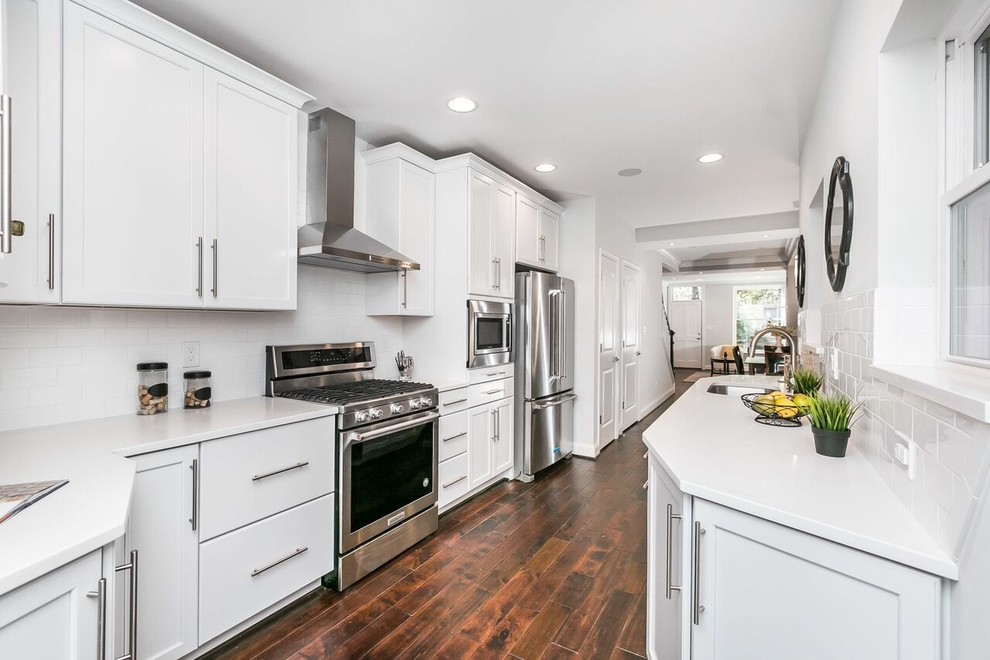 Enclosed kitchen - large transitional galley dark wood floor and brown floor enclosed kitchen idea in Baltimore with an undermount sink, recessed-panel cabinets, white cabinets, solid surface countertops, white backsplash, subway tile backsplash, stainless steel appliances, no island and white countertops
