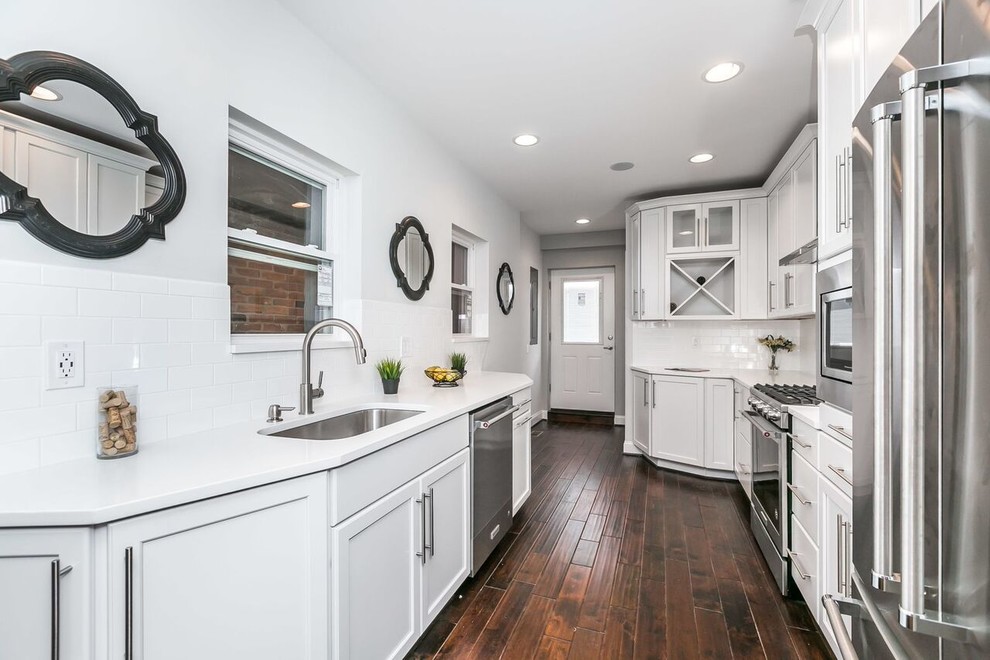 Inspiration for a mid-sized cottage galley dark wood floor and brown floor enclosed kitchen remodel in Baltimore with an undermount sink, shaker cabinets, white cabinets, solid surface countertops, white backsplash, subway tile backsplash, stainless steel appliances, no island and white countertops