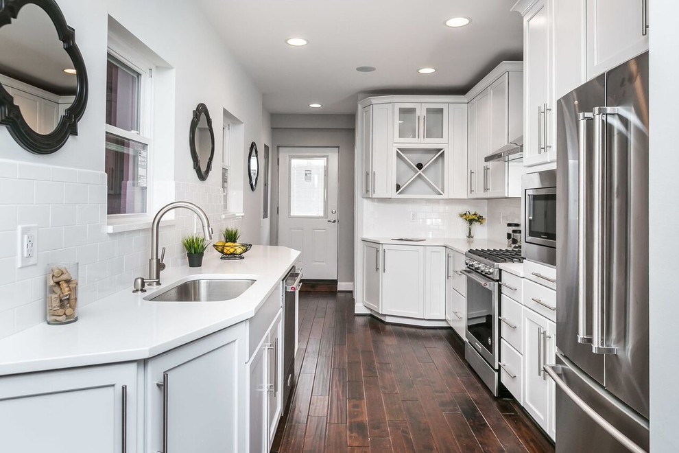 Inspiration for a mid-sized transitional galley dark wood floor and brown floor enclosed kitchen remodel in Baltimore with an undermount sink, shaker cabinets, white cabinets, solid surface countertops, white backsplash, subway tile backsplash, stainless steel appliances, no island and white countertops