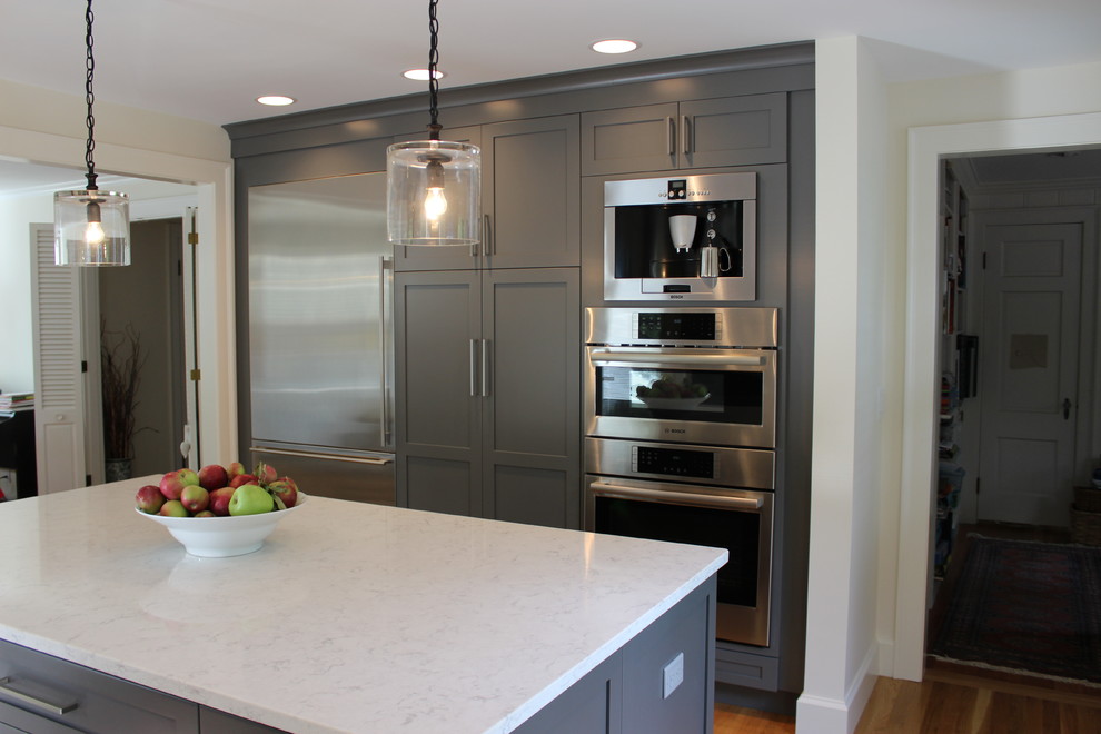 Inspiration for a medium sized classic u-shaped kitchen/diner in Boston with a single-bowl sink, recessed-panel cabinets, grey cabinets, engineered stone countertops, stainless steel appliances, light hardwood flooring and an island.