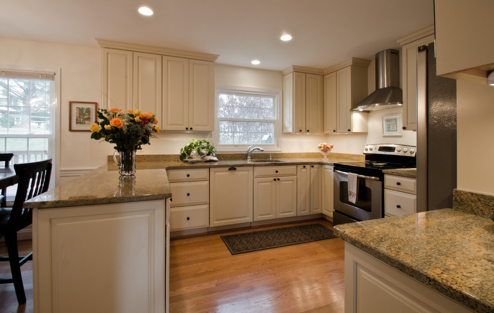 Klassisk inredning av ett avskilt, stort u-kök, med en undermonterad diskho, luckor med upphöjd panel, vita skåp, granitbänkskiva, rostfria vitvaror, ljust trägolv och en halv köksö