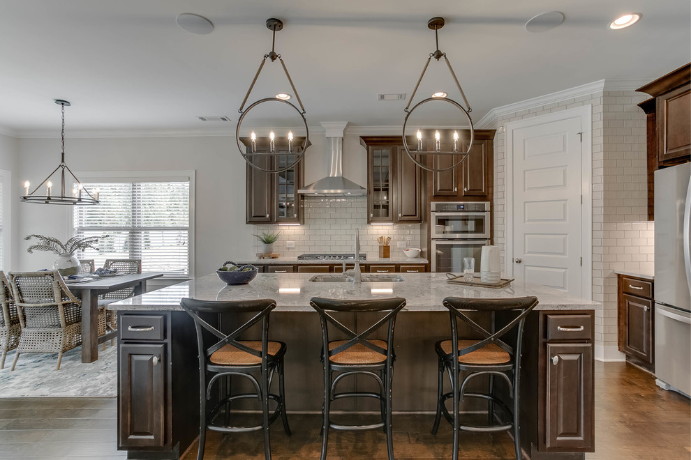 Exempel på ett klassiskt grå grått kök och matrum, med en undermonterad diskho, luckor med upphöjd panel, skåp i mörkt trä, vitt stänkskydd, stänkskydd i tunnelbanekakel, rostfria vitvaror, en köksö och brunt golv