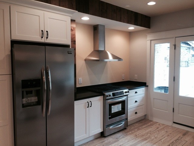Example of a mid-sized farmhouse l-shaped light wood floor eat-in kitchen design in Baltimore with a farmhouse sink, shaker cabinets, white cabinets, solid surface countertops, white backsplash, glass tile backsplash, stainless steel appliances and a peninsula