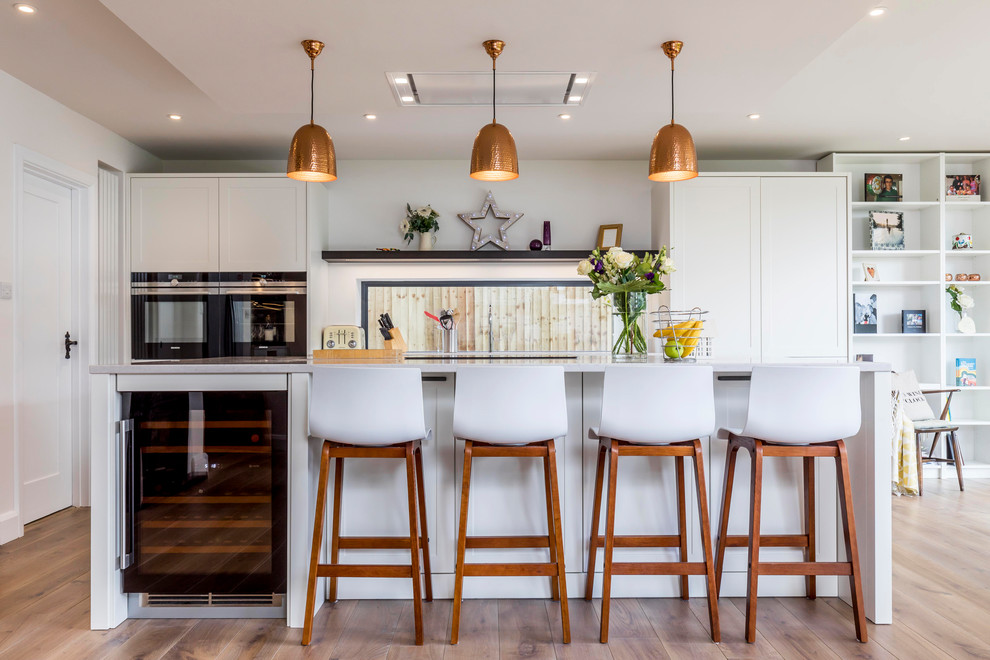 Mittelgroße, Zweizeilige Moderne Küche mit weißen Schränken, braunem Boden, Schrankfronten im Shaker-Stil, Rückwand-Fenster, braunem Holzboden und Kücheninsel in Sussex