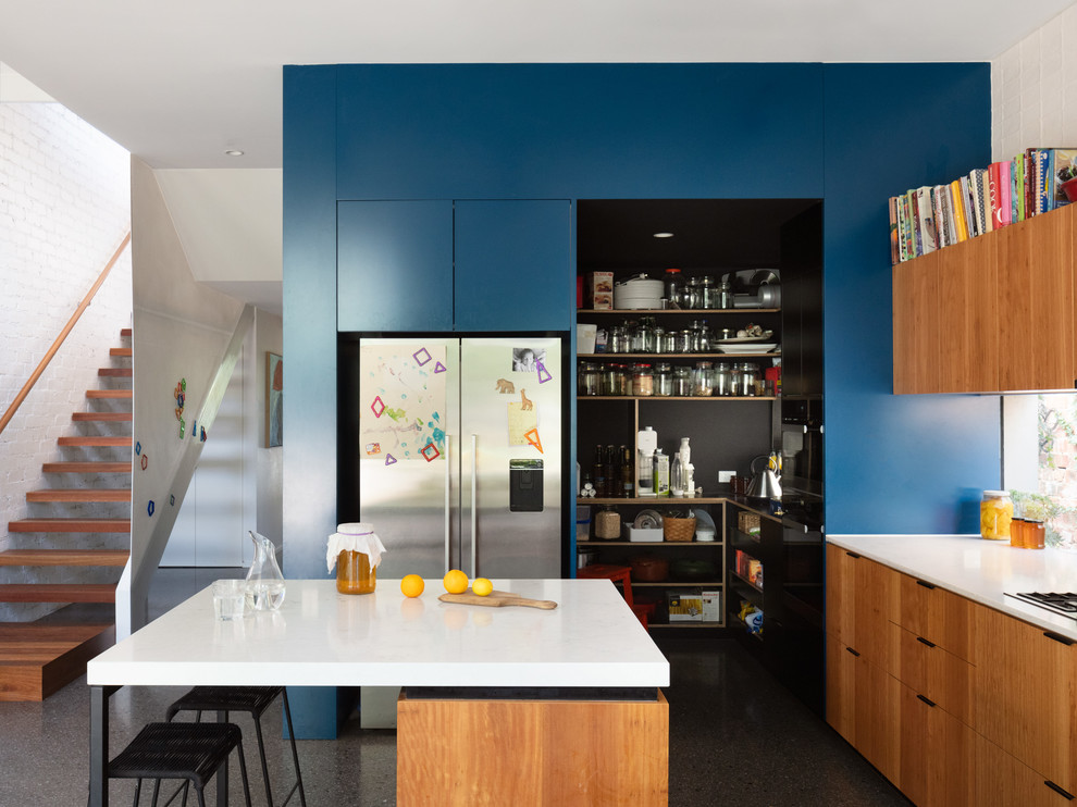 Moderne Küche mit flächenbündigen Schrankfronten, hellbraunen Holzschränken, Rückwand-Fenster, Küchengeräten aus Edelstahl, Betonboden, Kücheninsel, grauem Boden und weißer Arbeitsplatte in Melbourne