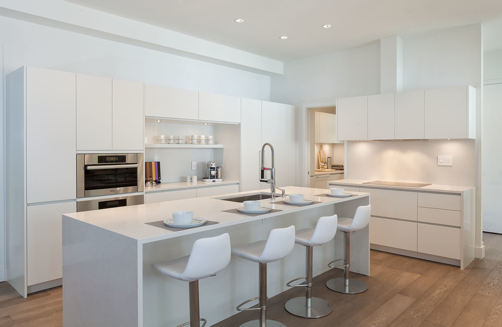 Trendy l-shaped medium tone wood floor kitchen photo in Vancouver with an undermount sink, flat-panel cabinets, white cabinets, quartzite countertops, white backsplash, paneled appliances and an island