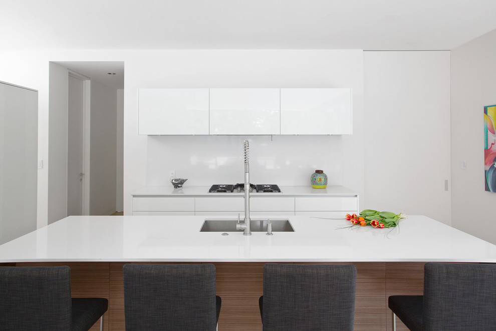 Cette image montre une cuisine minimaliste avec un évier encastré, un placard à porte plane, des portes de placard blanches et une crédence blanche.