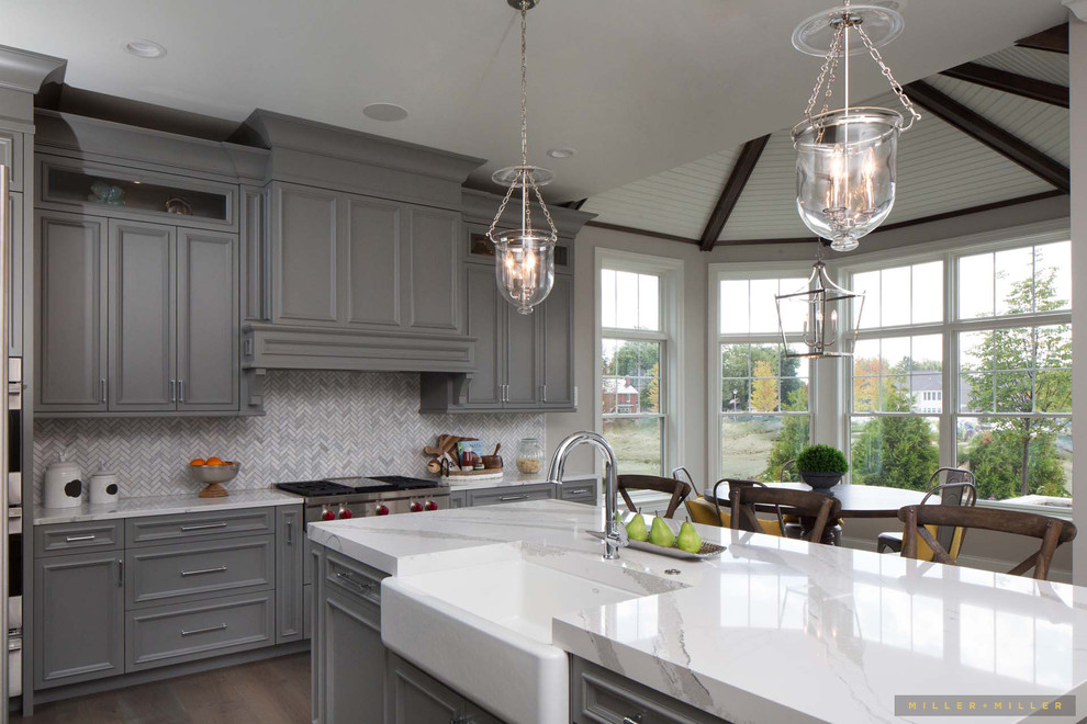 Photo of a large farmhouse l-shaped kitchen in Chicago with a belfast sink, beaded cabinets, grey cabinets, marble worktops, grey splashback, marble splashback, integrated appliances, medium hardwood flooring, an island, brown floors and white worktops.