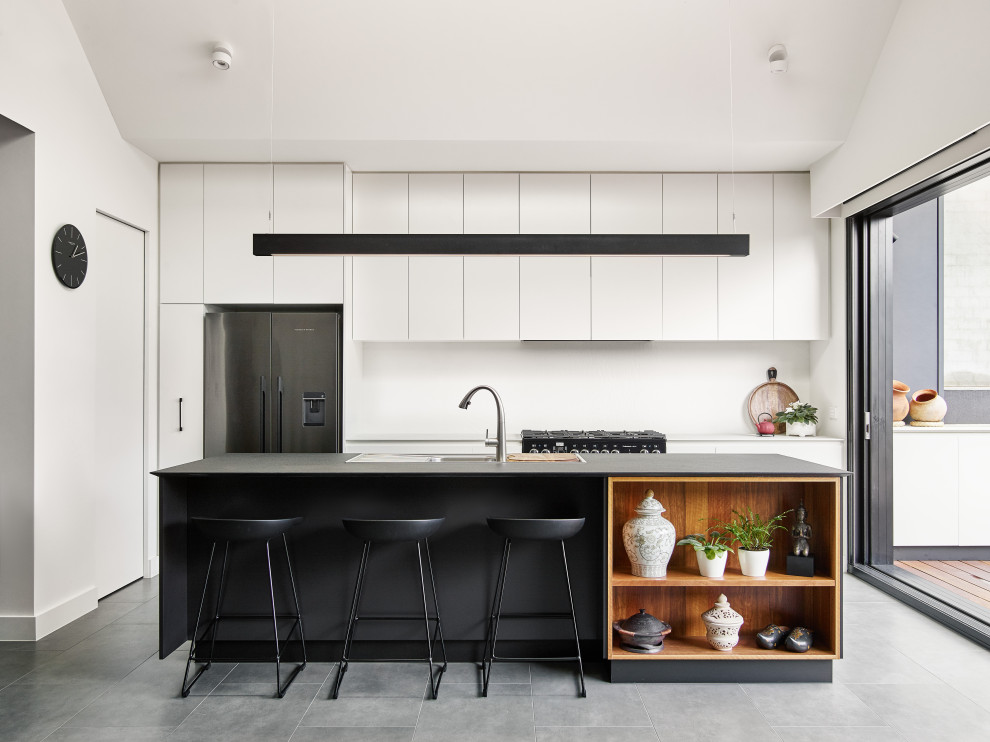 Inredning av ett modernt grå grått kök, med en nedsänkt diskho, släta luckor, vita skåp, rostfria vitvaror, en köksö, grått golv, bänkskiva i kvarts, vitt stänkskydd och cementgolv