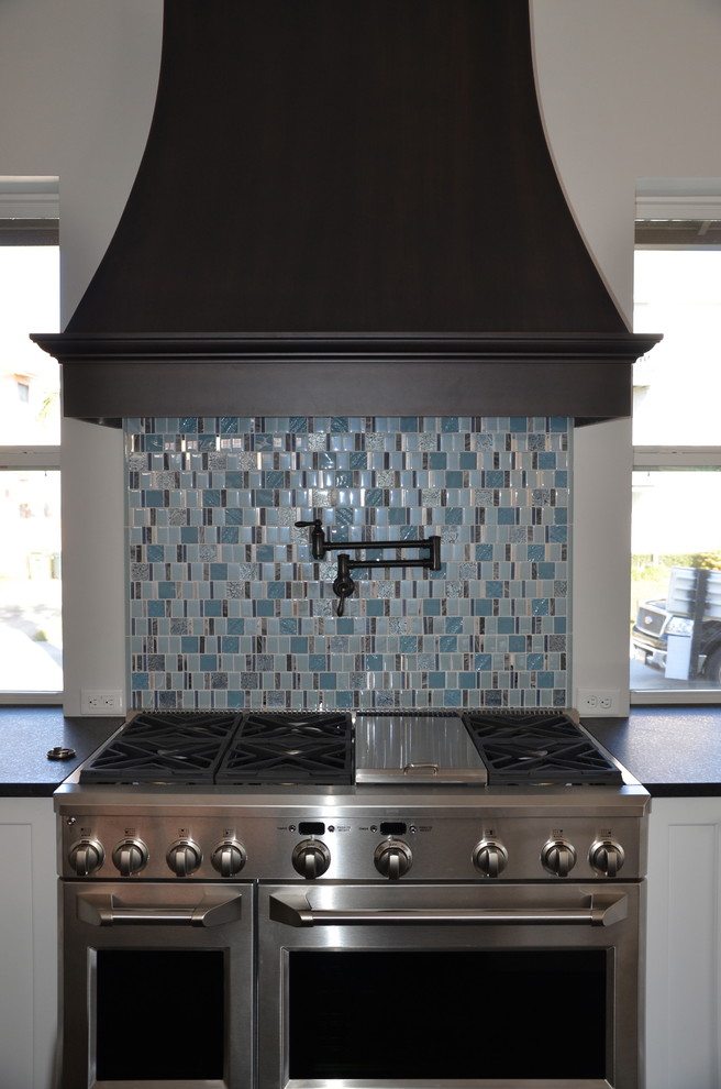 ジャクソンビルにあるエクレクティックスタイルのおしゃれなダイニングキッチン (茶色いキャビネット、青いキッチンパネル、ガラス板のキッチンパネル、シルバーの調理設備) の写真