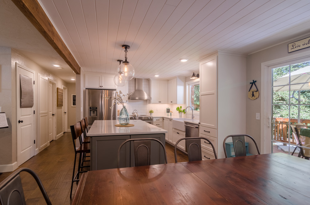 Inspiration for a small cottage l-shaped medium tone wood floor open concept kitchen remodel in Other with a farmhouse sink, shaker cabinets, white cabinets, quartz countertops, white backsplash, ceramic backsplash, stainless steel appliances, an island and white countertops