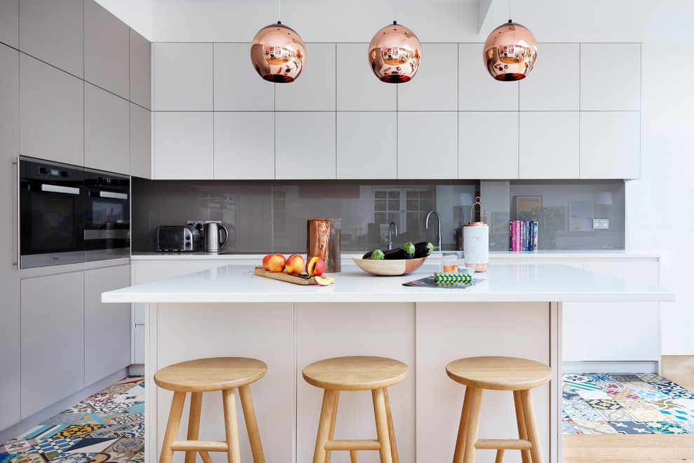 Moderne Küche in L-Form mit flächenbündigen Schrankfronten, weißen Schränken, Küchenrückwand in Grau, Glasrückwand, hellem Holzboden und Kücheninsel in London