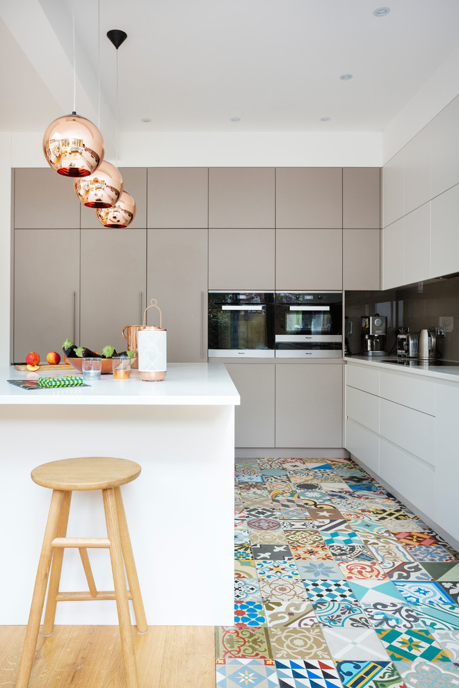 Design ideas for a contemporary l-shaped kitchen in London with flat-panel cabinets, white cabinets, grey splashback, glass sheet splashback, light hardwood flooring and an island.