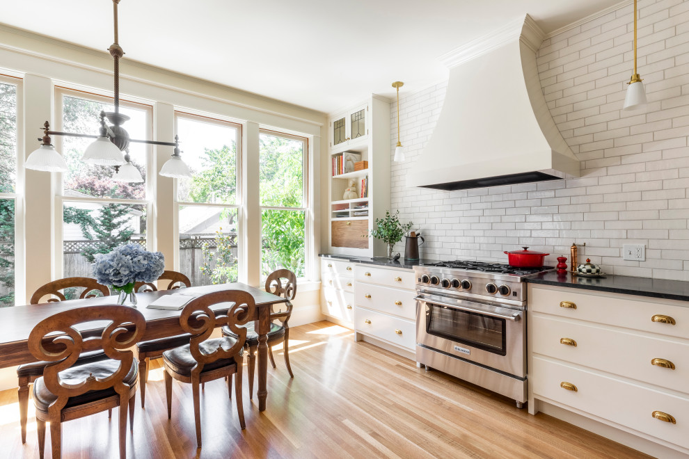 Kitchen - transitional medium tone wood floor and brown floor kitchen idea in Portland with white cabinets, soapstone countertops, white backsplash, brick backsplash, stainless steel appliances and black countertops