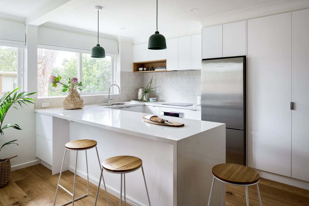 Inspiration for a small contemporary u-shaped kitchen/diner in Melbourne with a double-bowl sink, white cabinets, engineered stone countertops, beige splashback, ceramic splashback, stainless steel appliances, brown floors, white worktops, flat-panel cabinets, medium hardwood flooring and a breakfast bar.