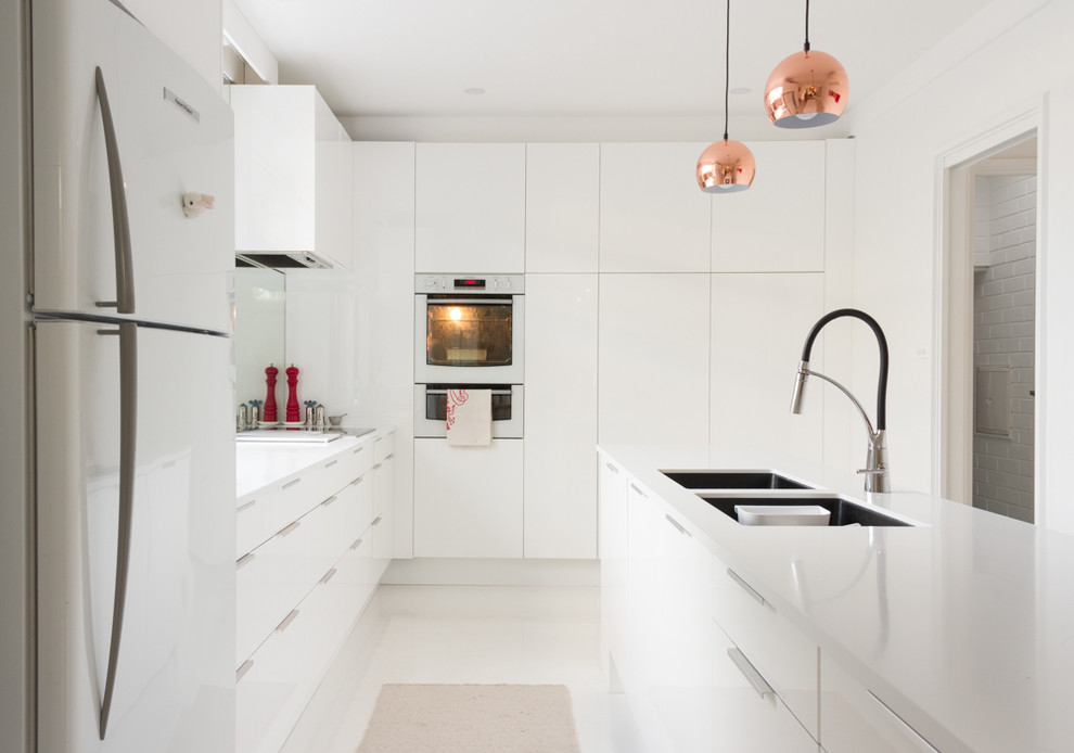 Trendy l-shaped porcelain tile kitchen pantry photo in Melbourne with an undermount sink, flat-panel cabinets, white cabinets, granite countertops, mirror backsplash, white appliances and an island