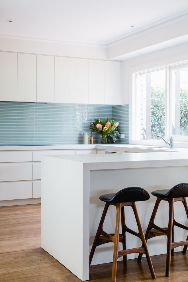 Mittelgroße Moderne Küche mit Vorratsschrank, hellen Holzschränken, Küchenrückwand in Blau, Rückwand aus Glasfliesen, schwarzen Elektrogeräten und braunem Boden in Melbourne