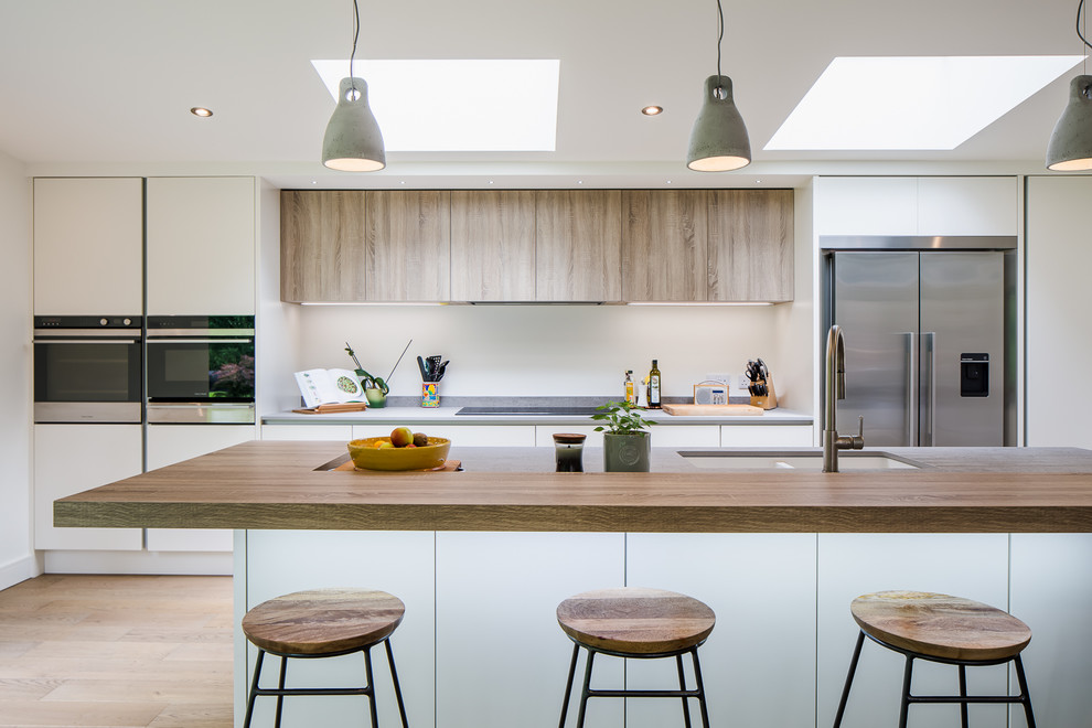 Photo of a contemporary kitchen in Other with a double-bowl sink, flat-panel cabinets, white cabinets, stainless steel appliances, light hardwood flooring, an island, beige floors and grey worktops.