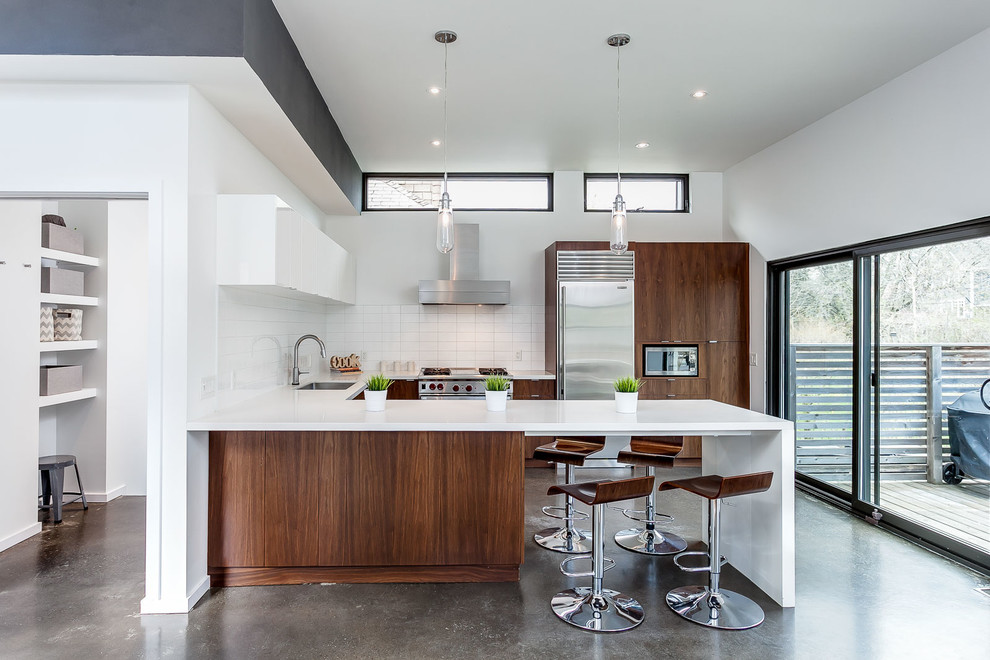 Open concept kitchen - mid-sized contemporary u-shaped concrete floor and gray floor open concept kitchen idea in Toronto with an undermount sink, flat-panel cabinets, dark wood cabinets, white backsplash, stainless steel appliances, a peninsula, solid surface countertops, ceramic backsplash and white countertops
