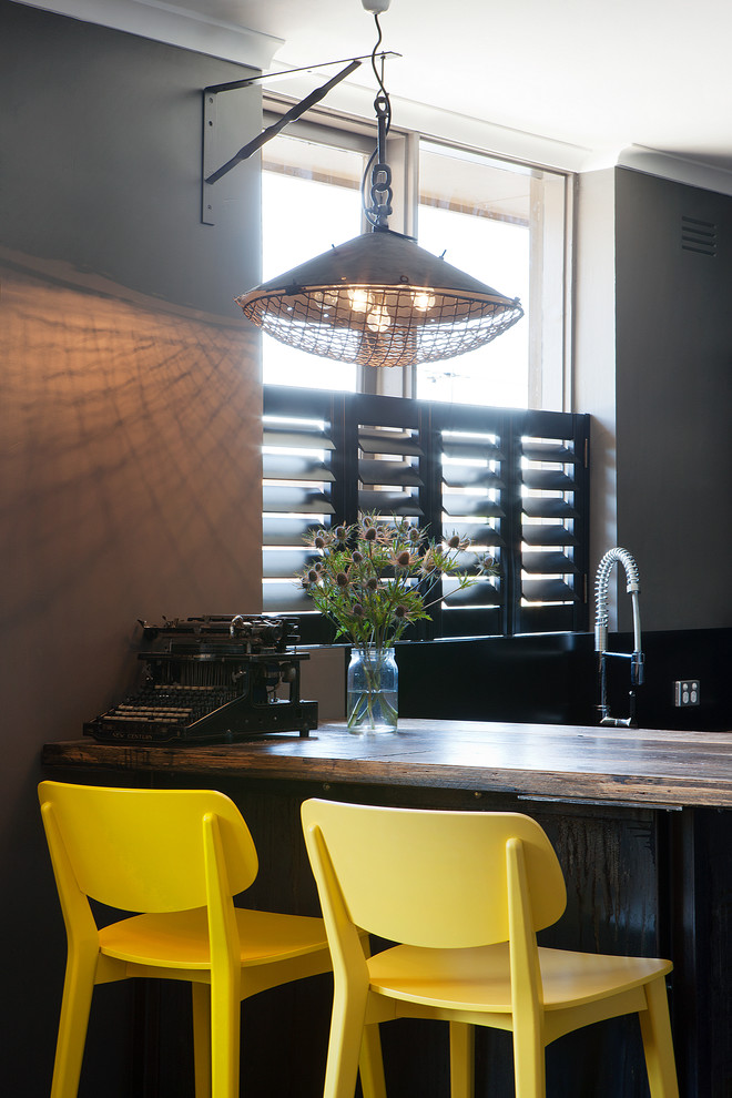 Photo of a small urban u-shaped kitchen/diner in Melbourne with a double-bowl sink, beaded cabinets, black cabinets, wood worktops, black splashback, stainless steel appliances, concrete flooring and an island.