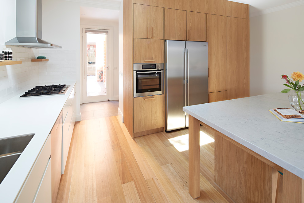 Photo of a large coastal single-wall open plan kitchen in Melbourne with a double-bowl sink, beaded cabinets, medium wood cabinets, marble worktops, stainless steel appliances, light hardwood flooring, an island, brown floors and white worktops.
