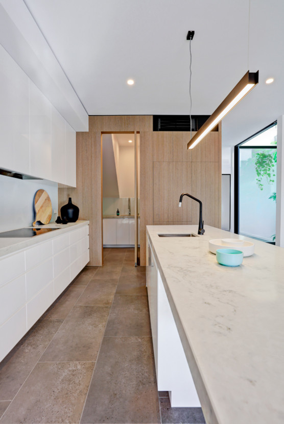 Modern inredning av ett stort grå grått kök, med en undermonterad diskho, vita skåp, bänkskiva i kvarts, vitt stänkskydd, glaspanel som stänkskydd, svarta vitvaror, klinkergolv i porslin, släta luckor, en köksö och brunt golv