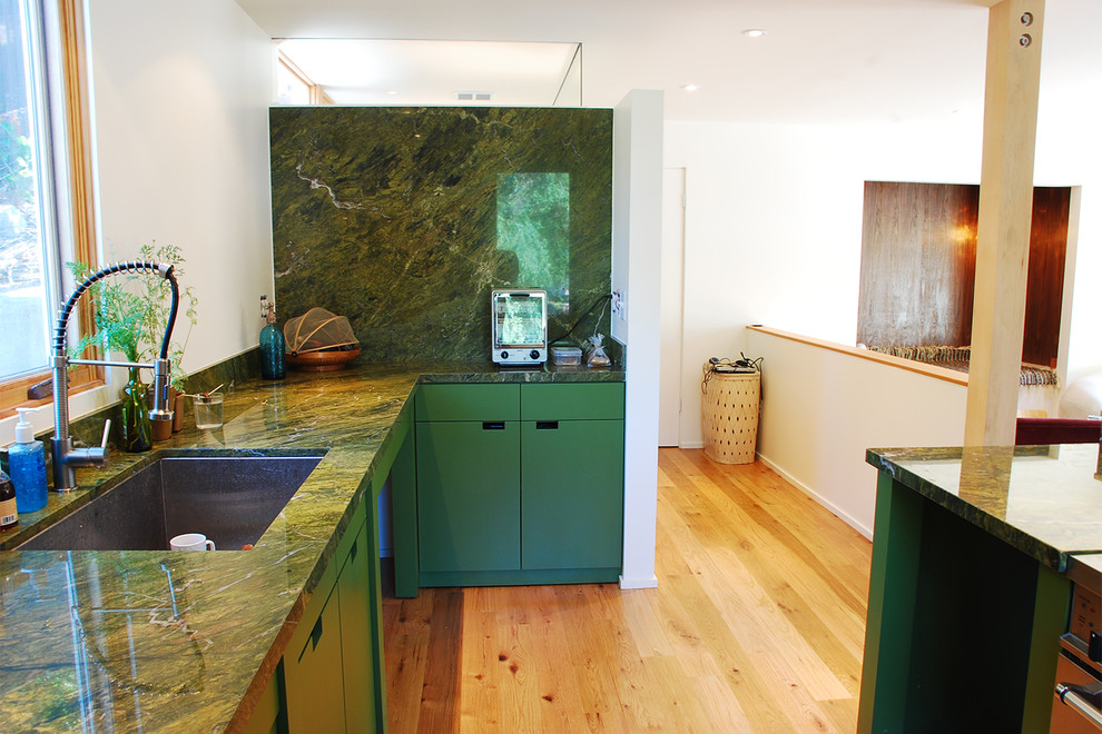 Large modern enclosed kitchen in Los Angeles with a submerged sink, flat-panel cabinets, green cabinets, onyx worktops, green splashback, window splashback, coloured appliances, light hardwood flooring, an island and beige floors.
