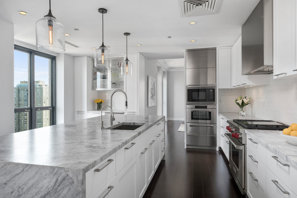 Moderne Küche mit weißen Schränken, Küchenrückwand in Weiß, Küchengeräten aus Edelstahl, Kücheninsel und braunem Boden in Chicago
