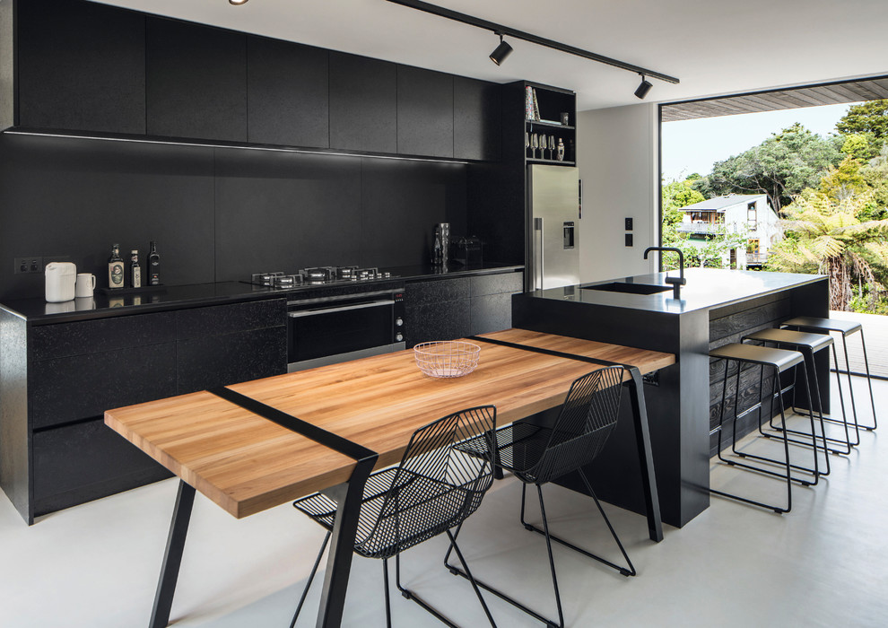 Пример оригинального дизайна: параллельная кухня в современном стиле с плоскими фасадами, черными фасадами, техникой из нержавеющей стали, бетонным полом, островом, серым полом и черной столешницей