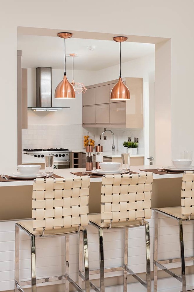 Design ideas for a contemporary u-shaped kitchen/diner in Dublin with flat-panel cabinets, brown cabinets, white splashback, metro tiled splashback, stainless steel appliances and an island.