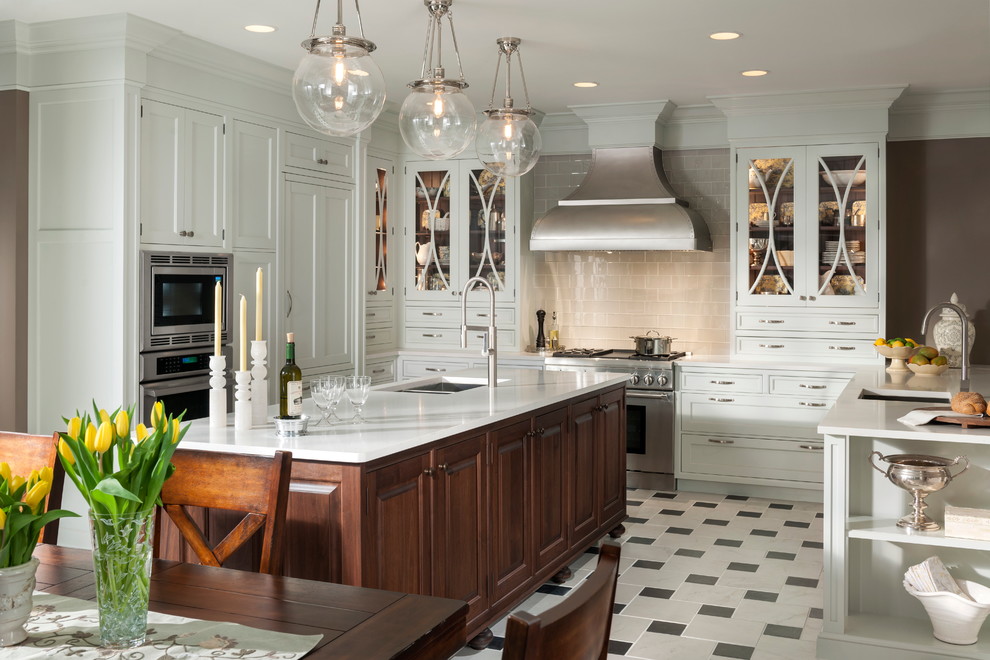 Exempel på ett klassiskt kök, med en undermonterad diskho, luckor med infälld panel, vita skåp, beige stänkskydd, stänkskydd i tunnelbanekakel, rostfria vitvaror, en köksö och marmorgolv