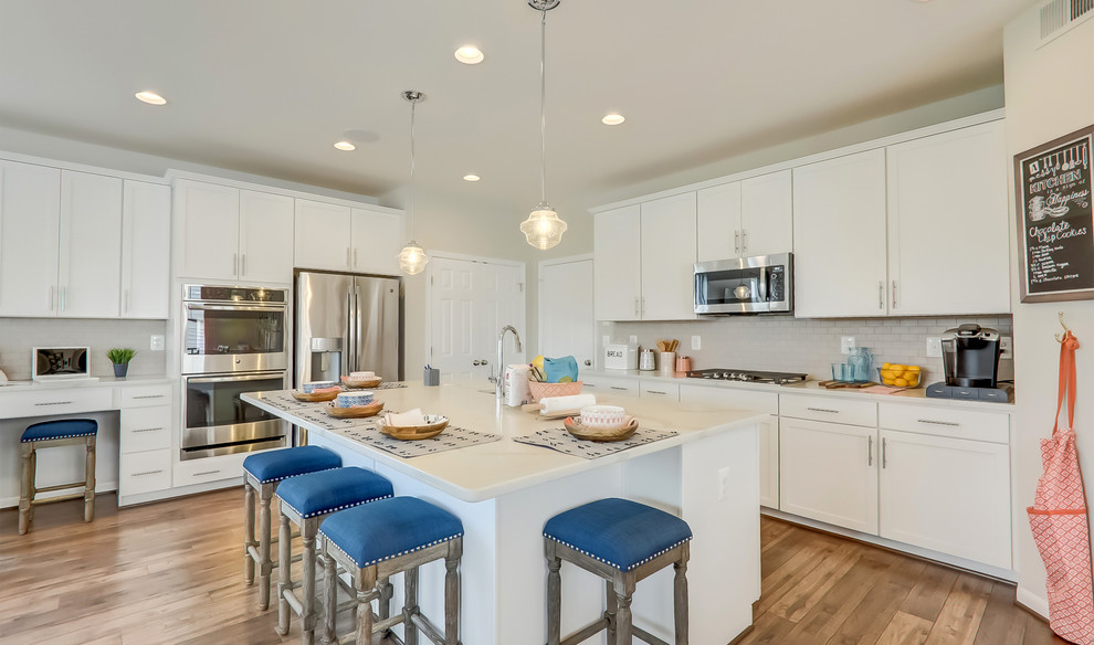 Example of a transitional l-shaped medium tone wood floor and brown floor kitchen design in DC Metro with an undermount sink, shaker cabinets, white cabinets, gray backsplash, stainless steel appliances, an island and white countertops