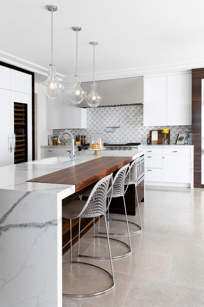 Modern inredning av ett mellanstort vit vitt kök, med en undermonterad diskho, släta luckor, vita skåp, bänkskiva i kvarts, flerfärgad stänkskydd, stänkskydd i glaskakel, integrerade vitvaror, kalkstensgolv, en köksö och grått golv
