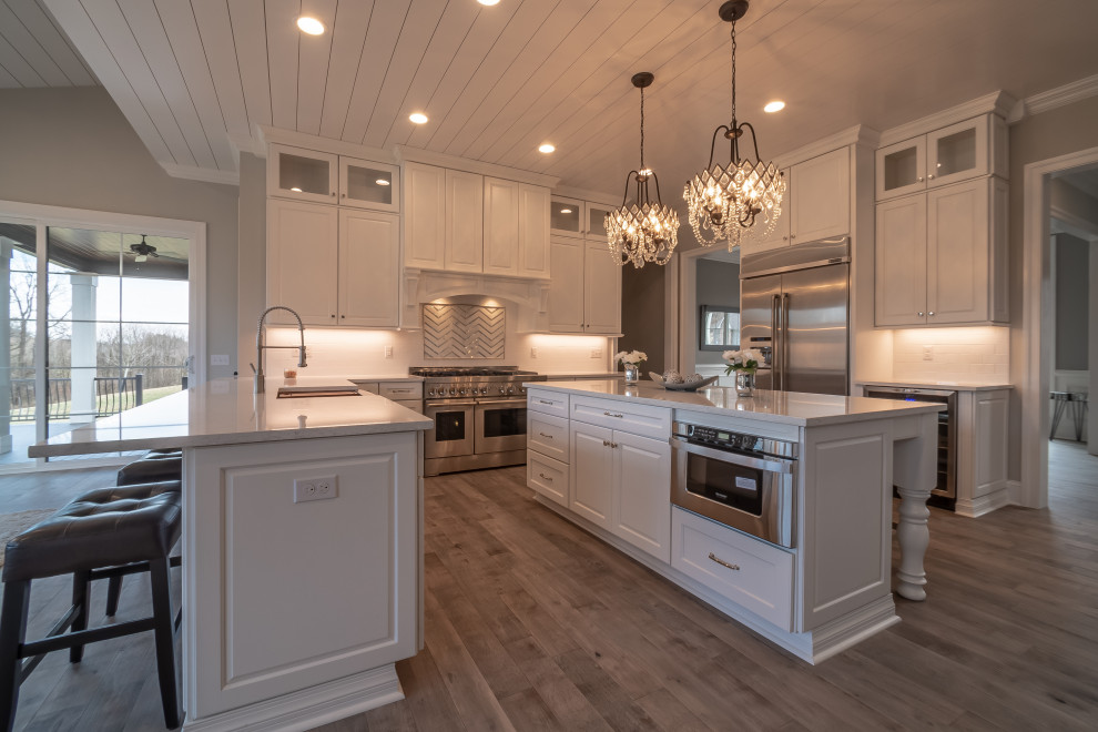 Kitchen - large shabby-chic style l-shaped light wood floor and shiplap ceiling kitchen idea in Other with a farmhouse sink, raised-panel cabinets, white cabinets, quartz countertops, white backsplash, stainless steel appliances, two islands and white countertops